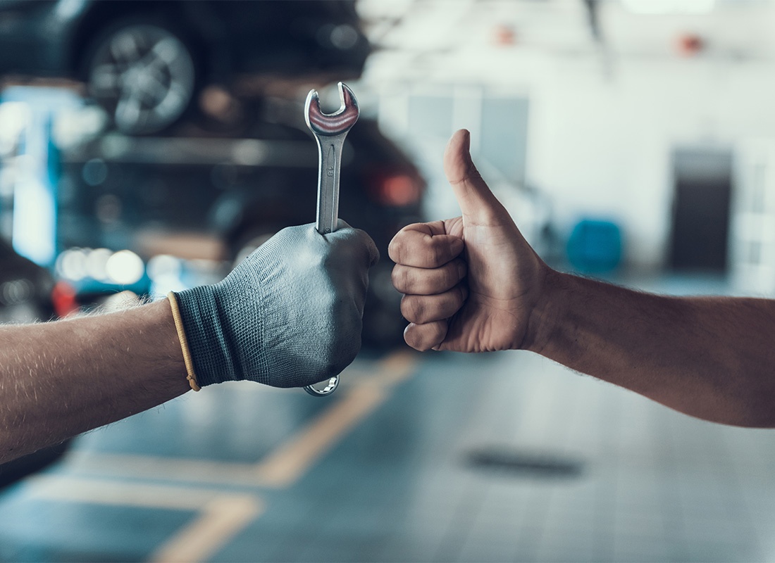 Auto Claims - Closeup View of a Mechanic Holding a Wrench in his Hand and a Client Giving him a Thumbs Up as They Stand in an Auto Repair Shop