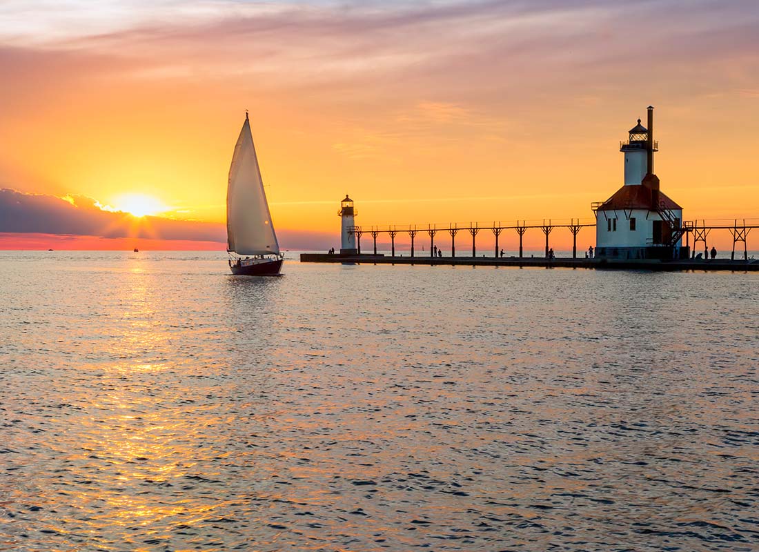 Blog - View of a Sailboat on the Ocean Near a Lighthouse Against a Colorful Sunset Sky
