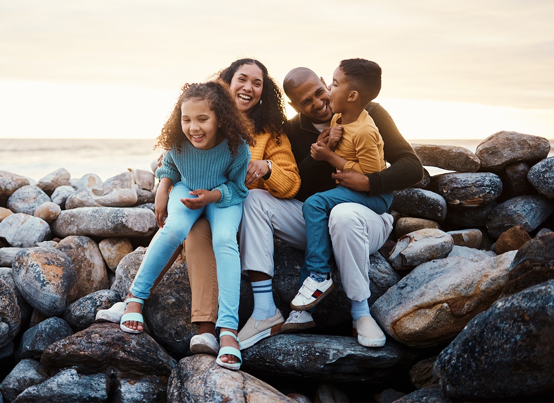 Read Our Reviews - Son and Daughter Having Fun Sitting on Their Parents Laps as They Spend Time Together Sitting on a Rock Jetty at the Beach